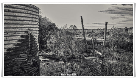 a black and white photo of a rusted water tank in a desolate landscape