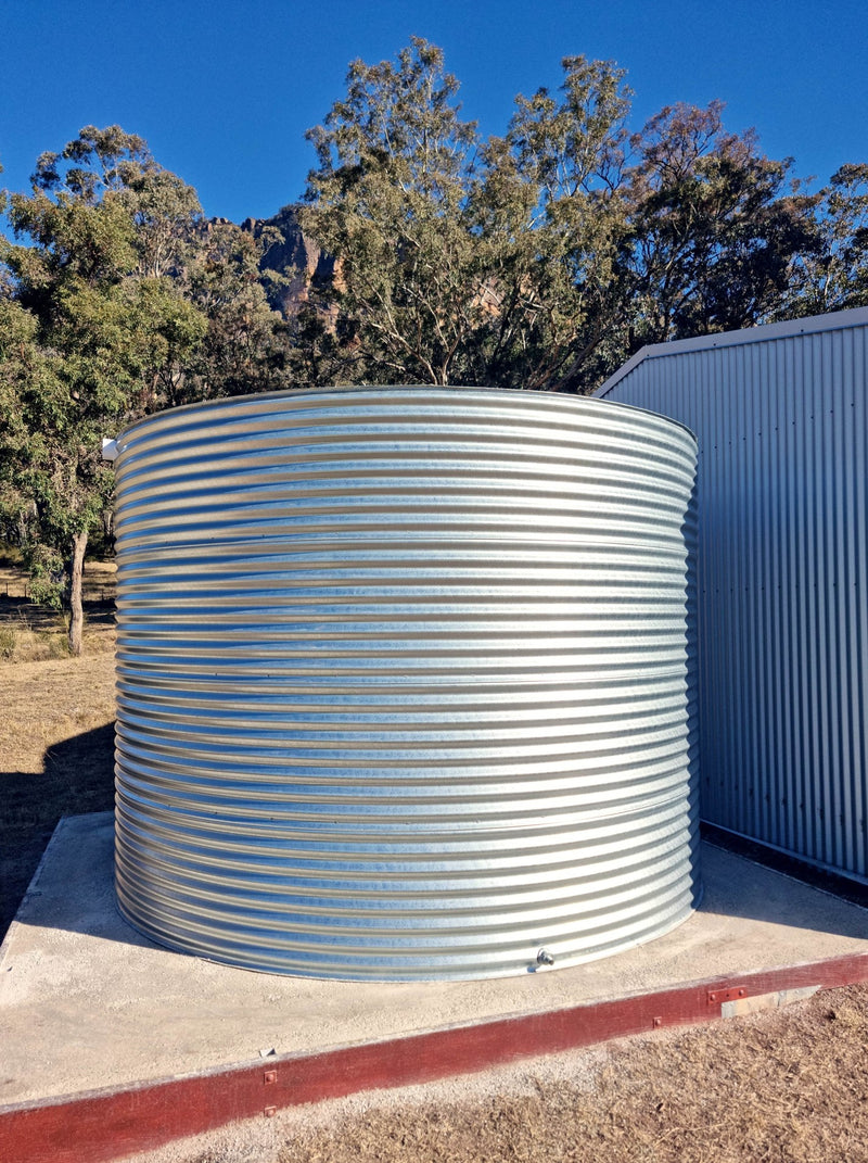 a galvanised round water tank on a good compressed pad next to an on old shed and in front of a mountain